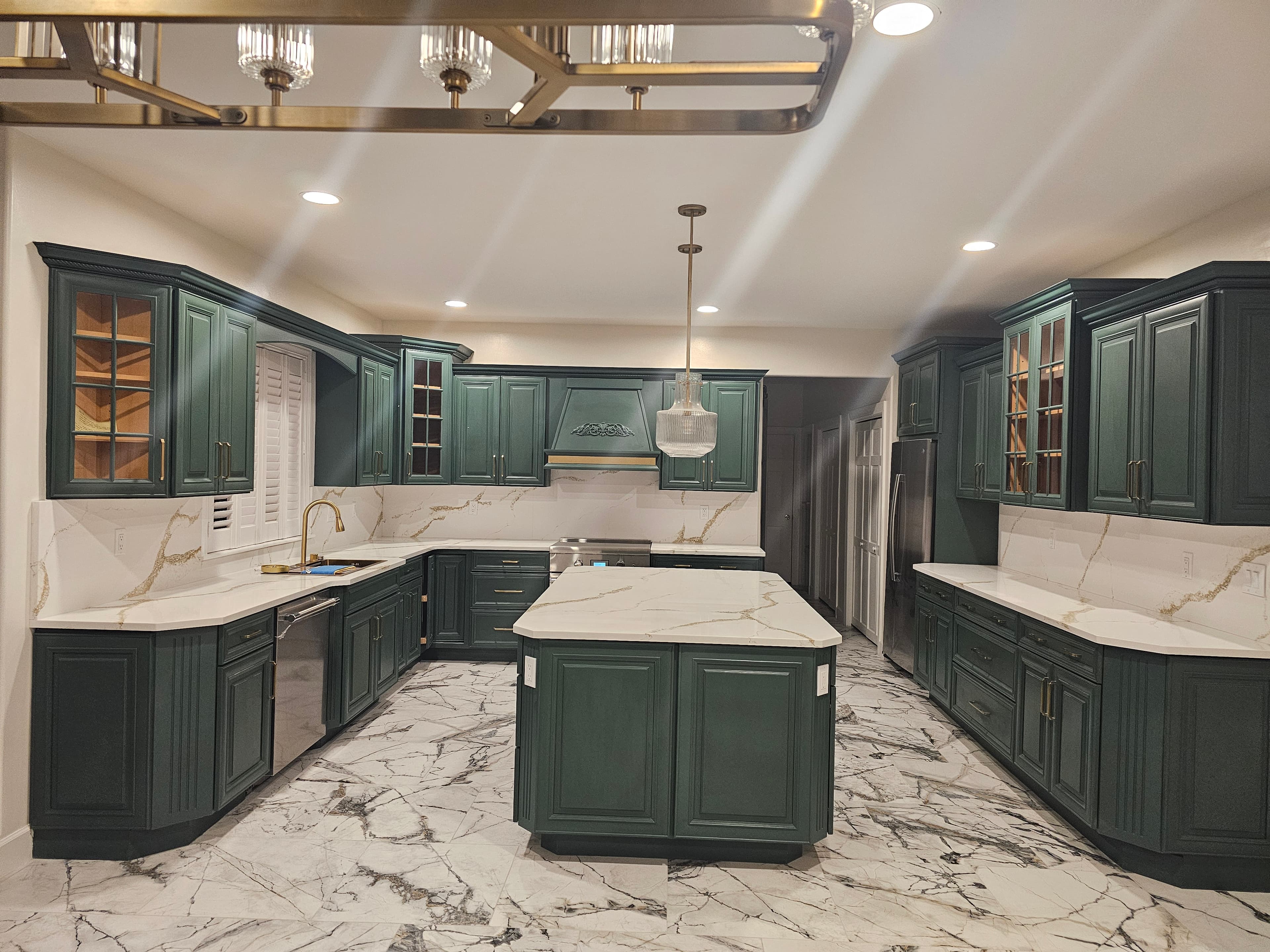 Modern kitchen featuring dark green cabinets, gold hardware, white marble countertops, and marble flooring.
