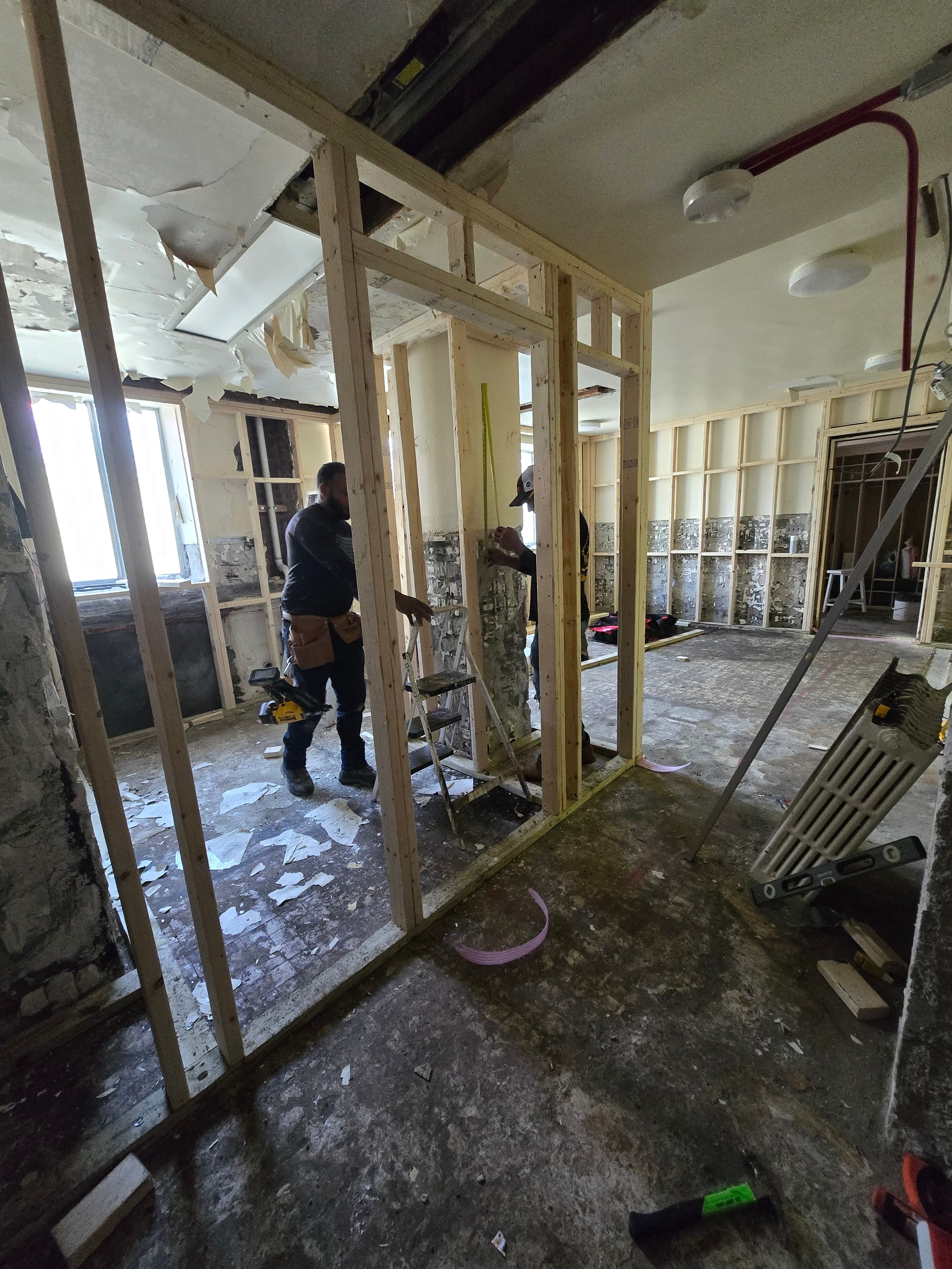 Construction worker installing wooden wall studs during an interior renovation project with scattered debris.