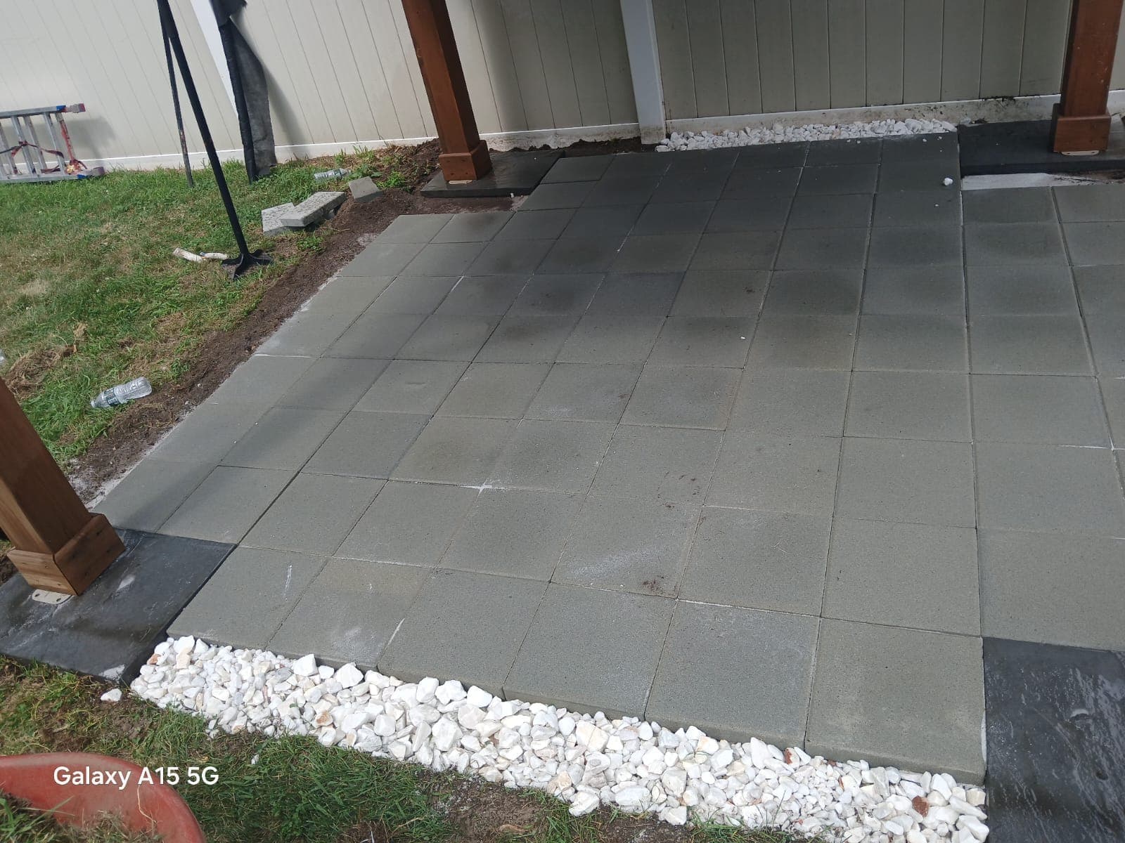 Gray square pavers create a patio area bordered by white stones and wooden support beams.